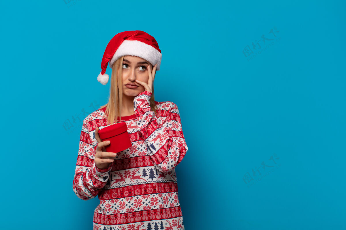成人戴着圣诞帽的金发女人在一项无聊 乏味 乏味的任务后 手捧着脸 感到无聊 沮丧和困倦睡眠圣诞节思考