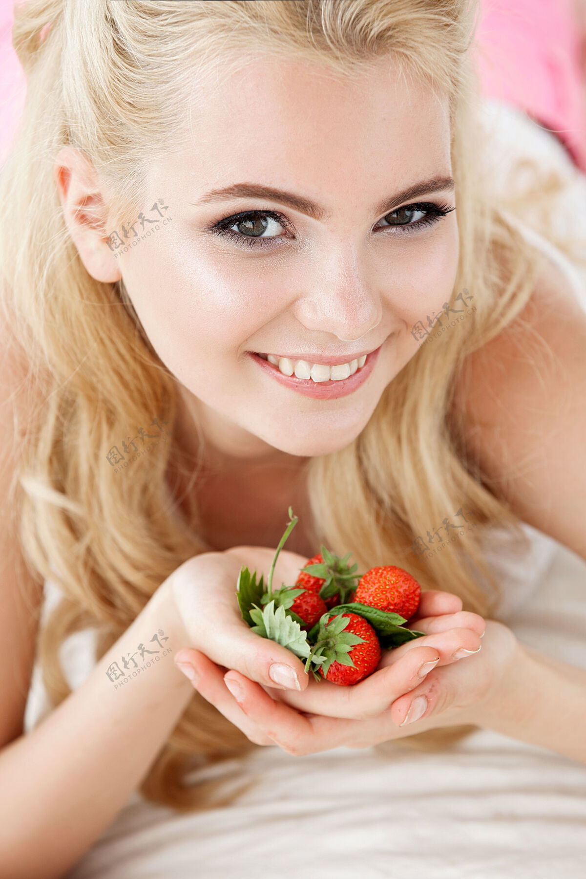 睡觉时间美丽的年轻微笑的女人坐在白色的床上 手里拿着一束野草莓卧室房间生活方式