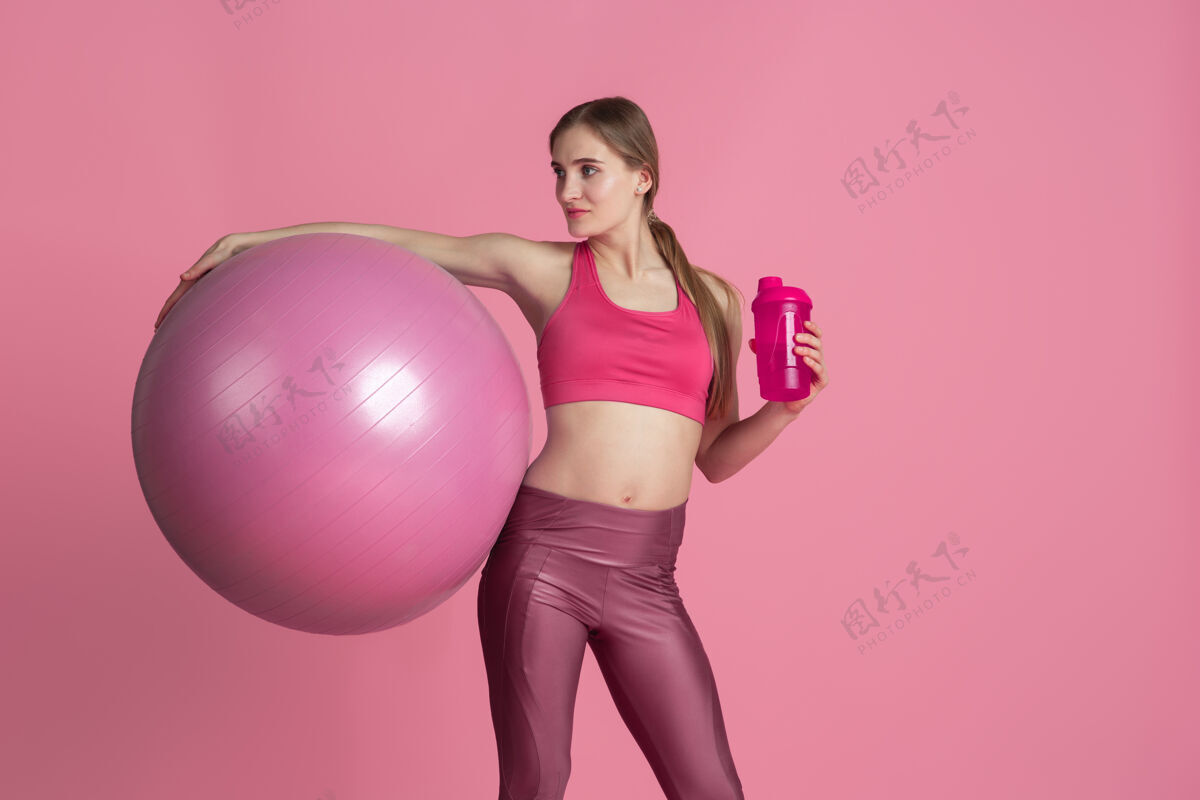 人美丽的年轻女运动员在粉色工作室墙上练习单色肖像女性锻炼一