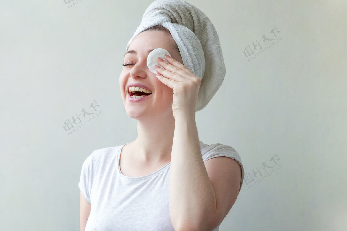 应用头上戴着毛巾的微笑女人的美丽肖像 柔软健康的皮肤 用隔离在白色背景上的化妆棉卸妆清洁删除制造