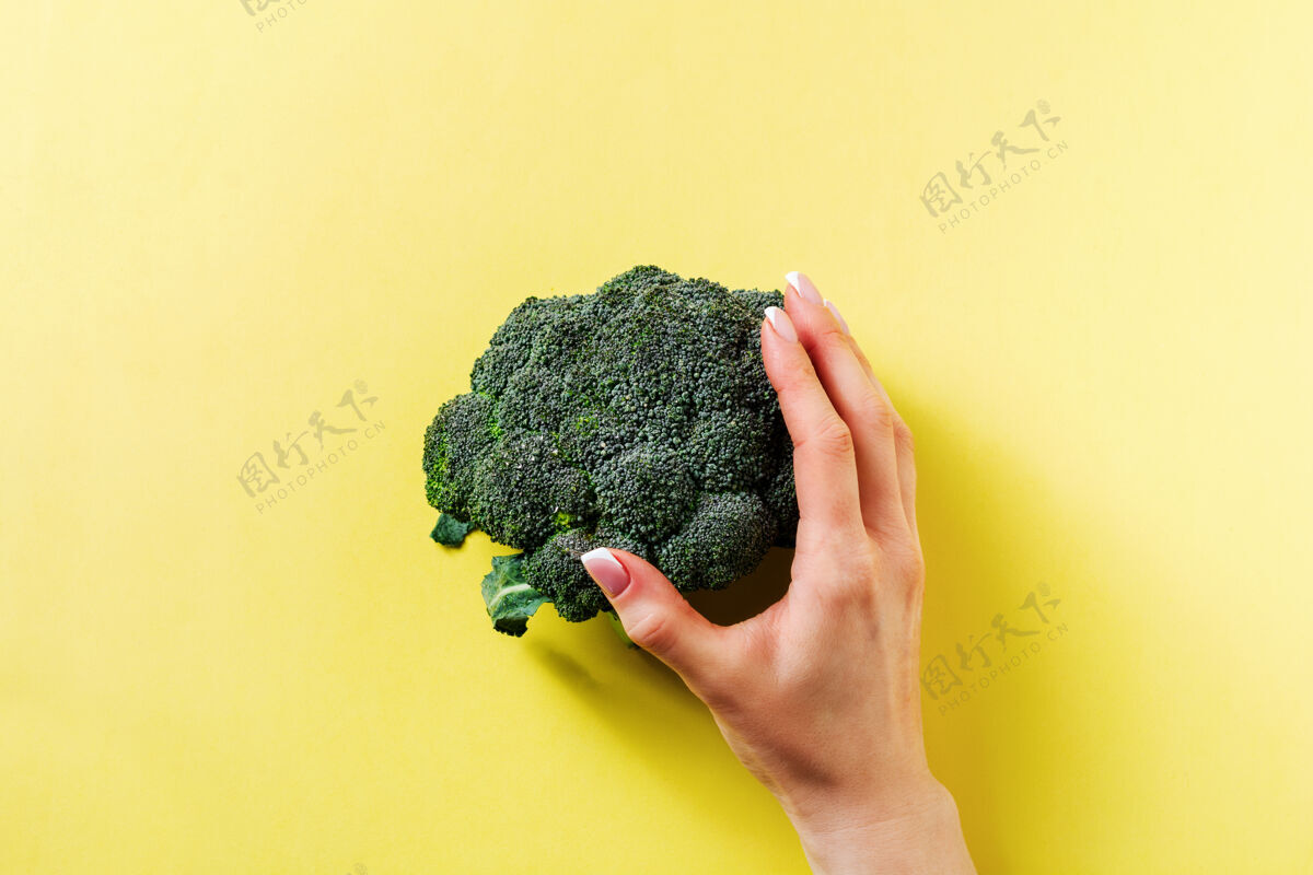 素食主义者雌性的手拿着一个新鲜的绿花椰菜躺在黄色的灯光下茎素食主义者沙拉