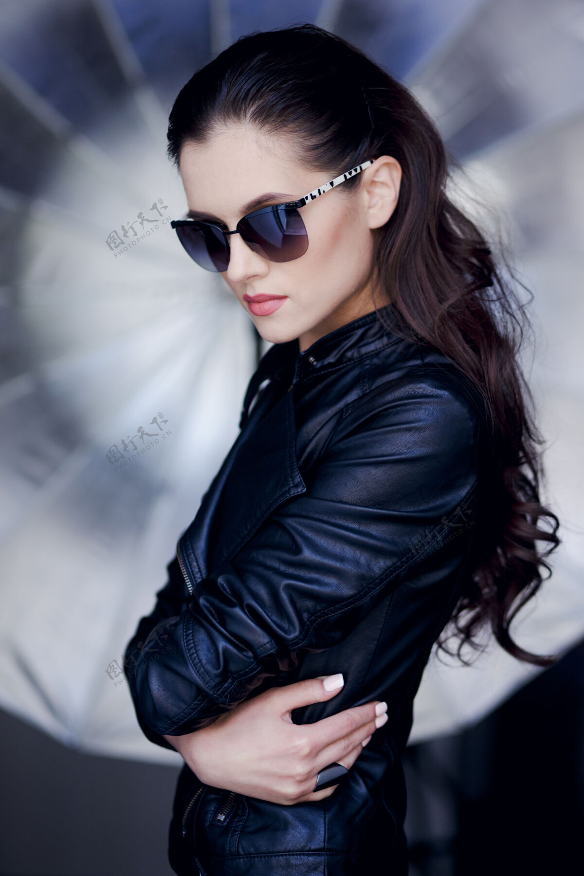 女孩自信和性感的年轻黑发女子摆出黑色皮夹克和太阳镜时尚发型皮革