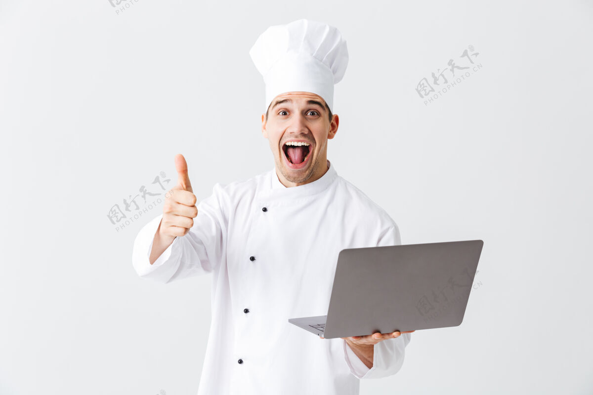 厨师开朗的厨师穿着制服站在白色的墙上 手里拿着笔记本电脑美食家互联网服务