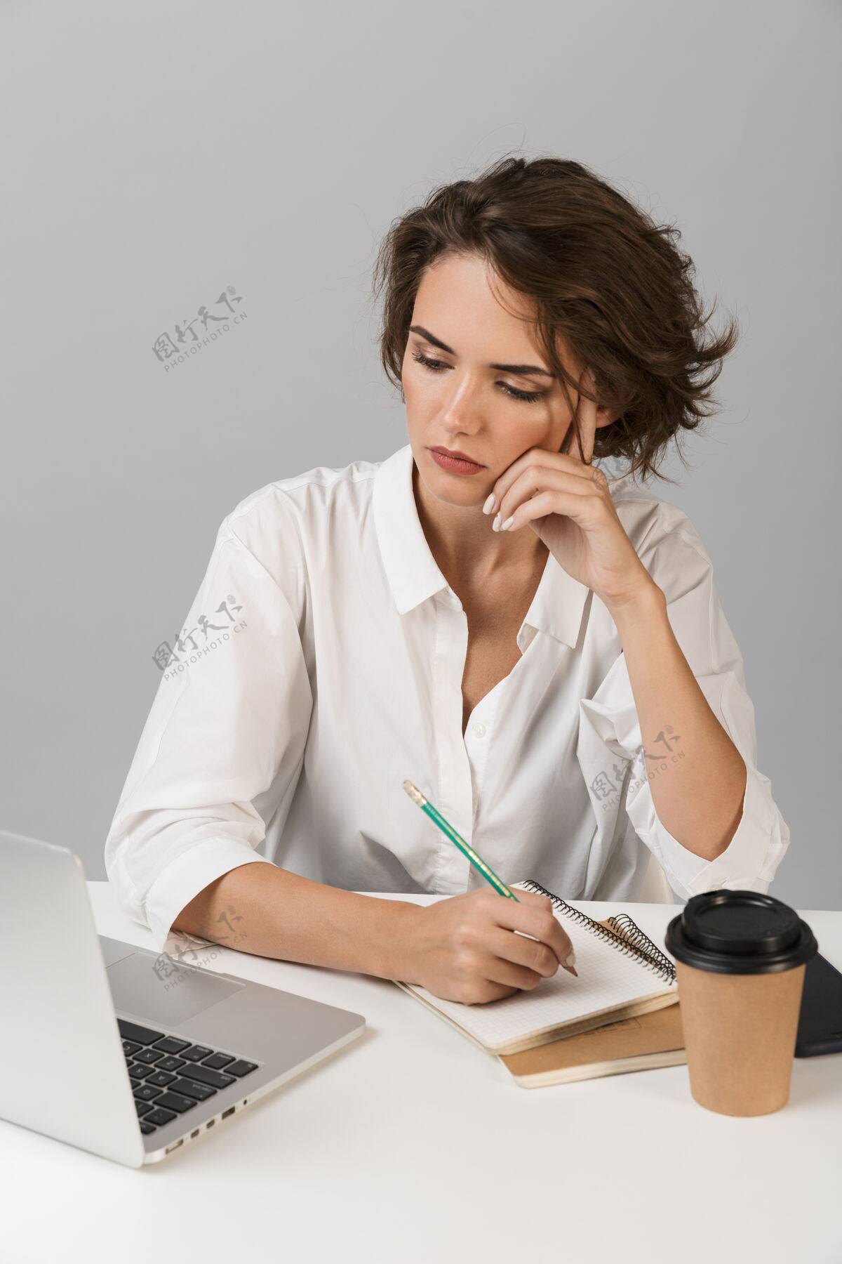 笔记本电脑严肃的女商人坐在桌旁用笔记本电脑隔着灰墙摆出孤立的姿势可爱年轻商务人士