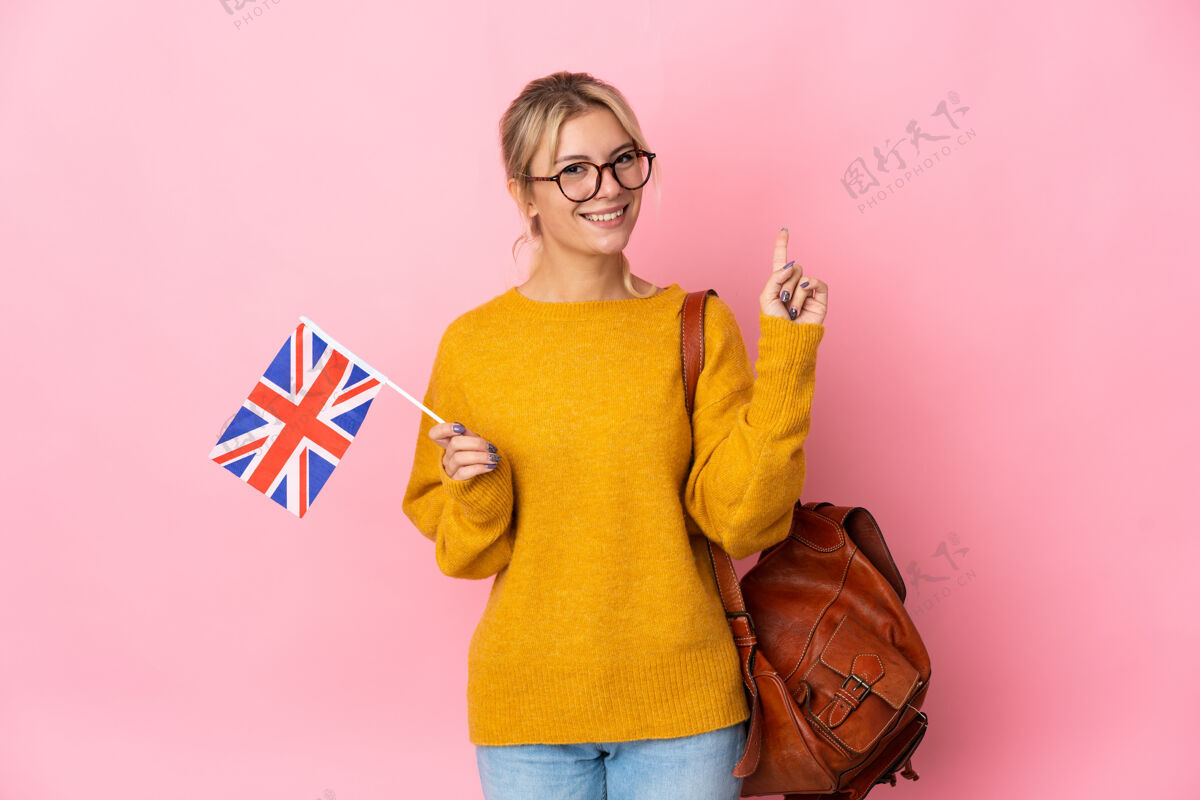人年轻的俄罗斯女子举着英国国旗 在粉红色背景下展示并举起手指表示最好的象征女女学生