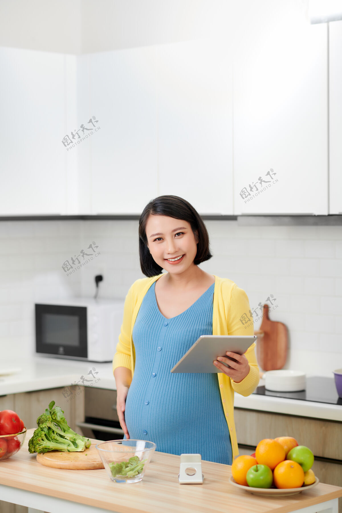 有机微笑的年轻孕妇在厨房做饭时使用数字平板电脑平板电脑厨房孕妇