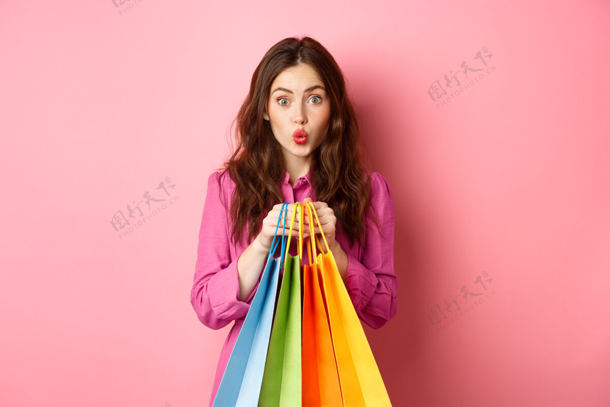 休闲迷人的女孩拿着购物袋 撅着嘴唇 面带羞怯 站在粉红色的墙上情绪候选人女性