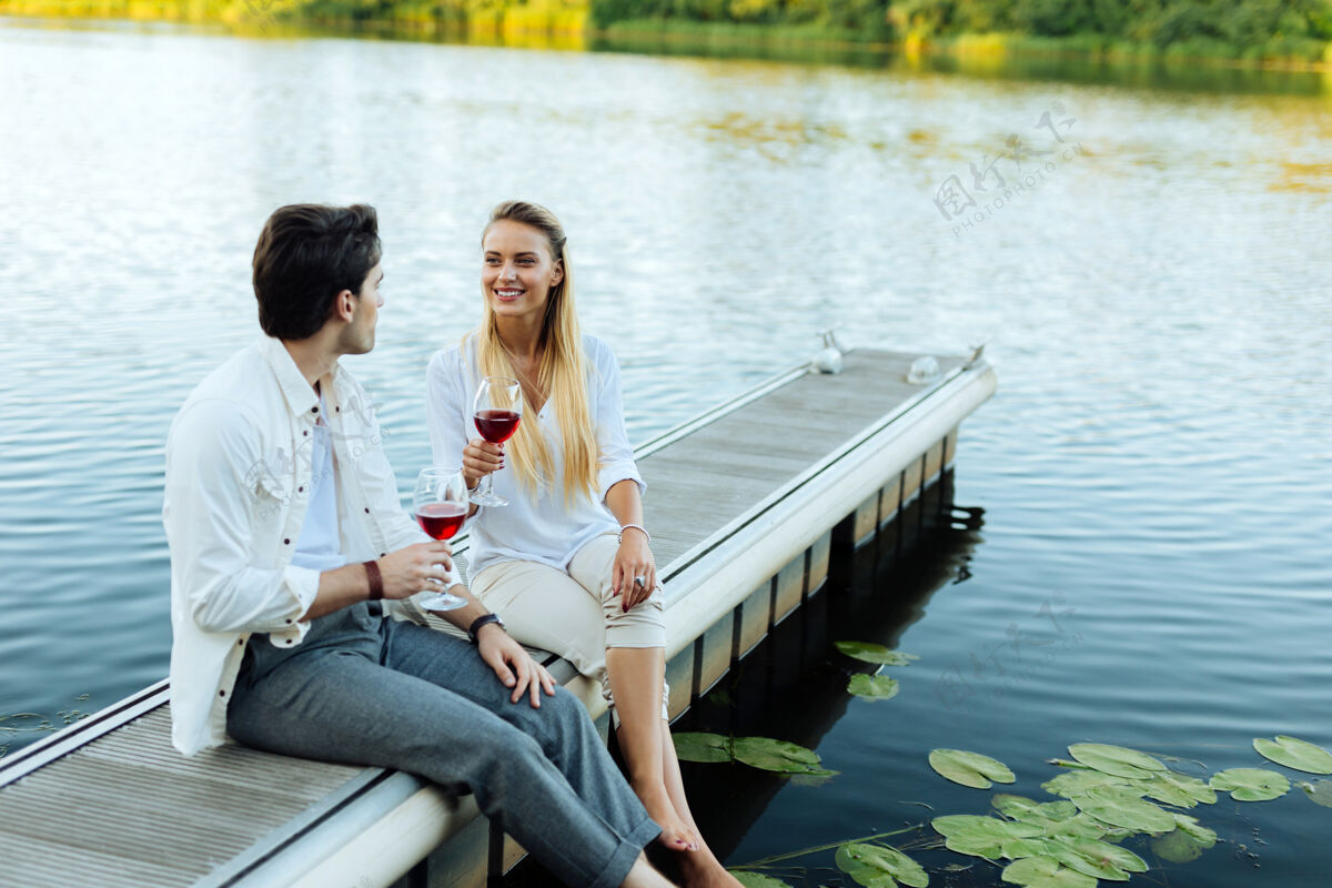 爱好浪漫的地方快乐的夫妇坐在河边 一边享受他们的葡萄酒交流放松关系