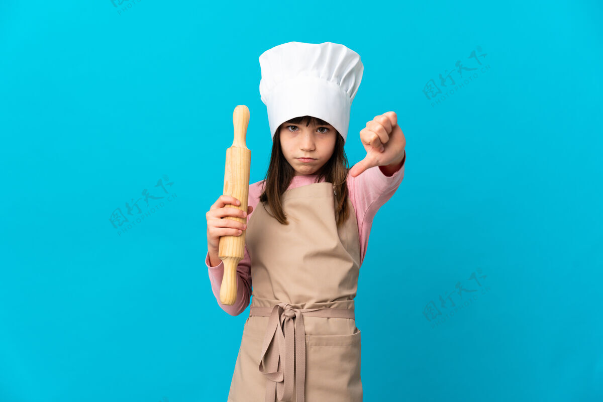 站一个拿着擀面杖的小女孩站在蓝色的墙上 拇指朝下 表情消极面包师围裙别针
