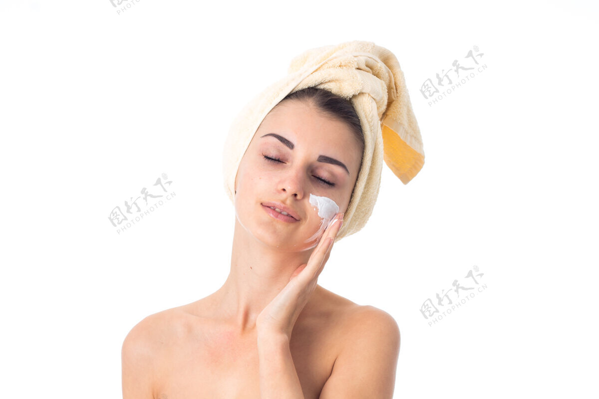 水疗美丽的女人用毛巾在头上涂上隔离在白墙上的霜来护理她的皮肤特写美丽健康