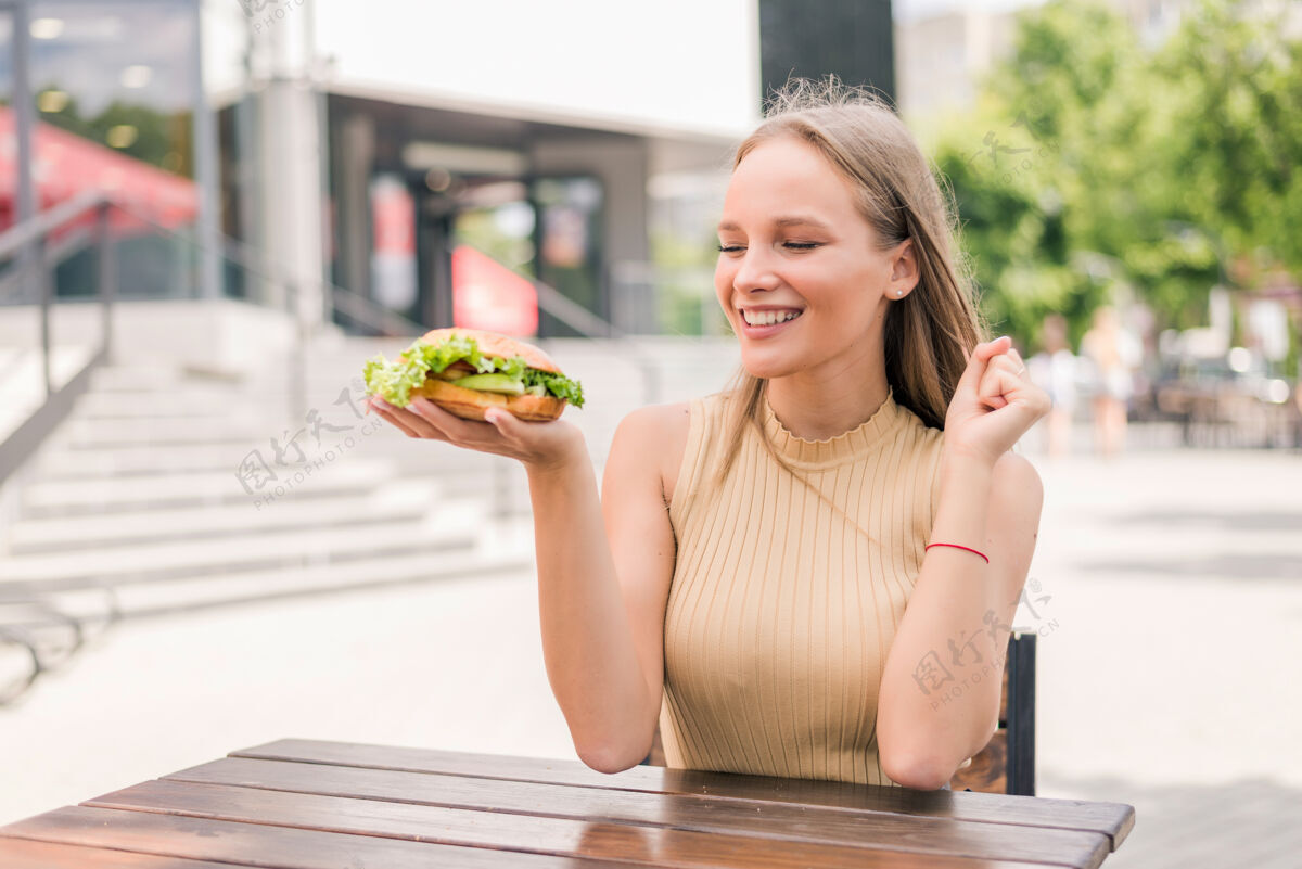 人年轻兴奋的女人快乐地抱着汉堡包坐在户外休息饥饿嘴巴