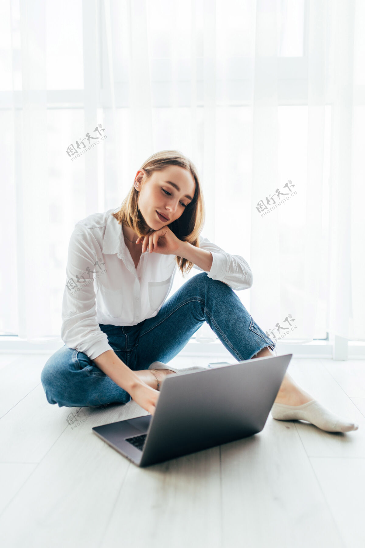 室内漂亮的年轻女子坐在地板上用笔记本电脑冲浪可爱家庭女性