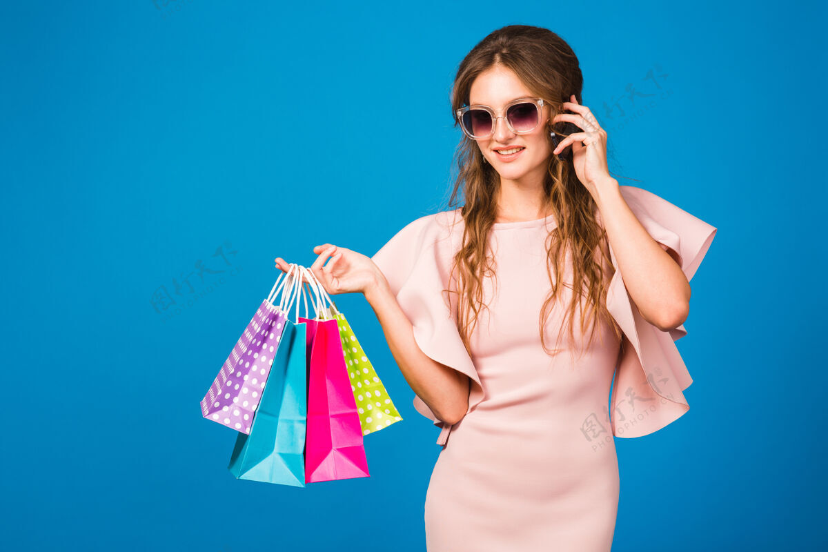 购物者穿着粉色豪华连衣裙 手持购物袋 手拿手机的年轻时尚美女奢侈品服装女人