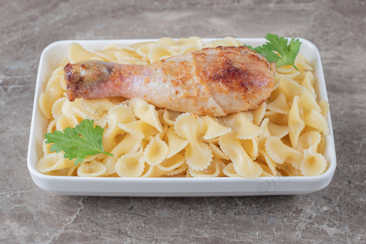 美味把鸡腿放在碗里的意大利面上 放在大理石表面上美味鸡腿美味