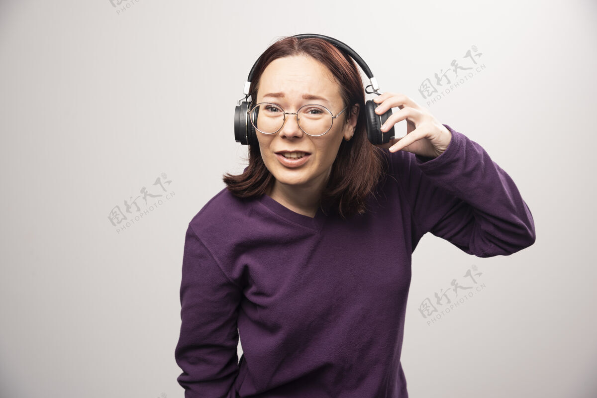 模特戴着眼镜的年轻女子戴着耳机在听音乐 这是一张高质量的白色照片人类肖像站立