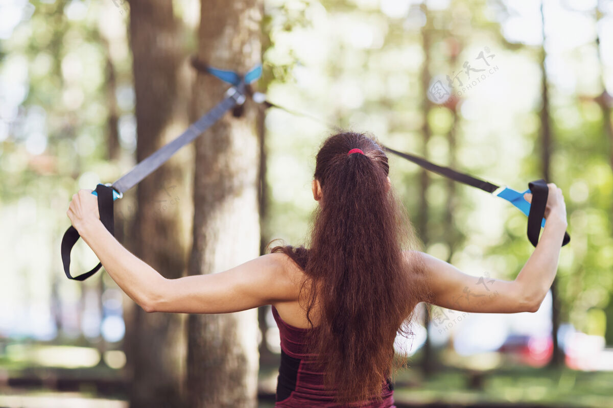 教练一位年轻女子在公园里的一棵树上的高架机器上锻炼背部肌肉磁带运动员女人