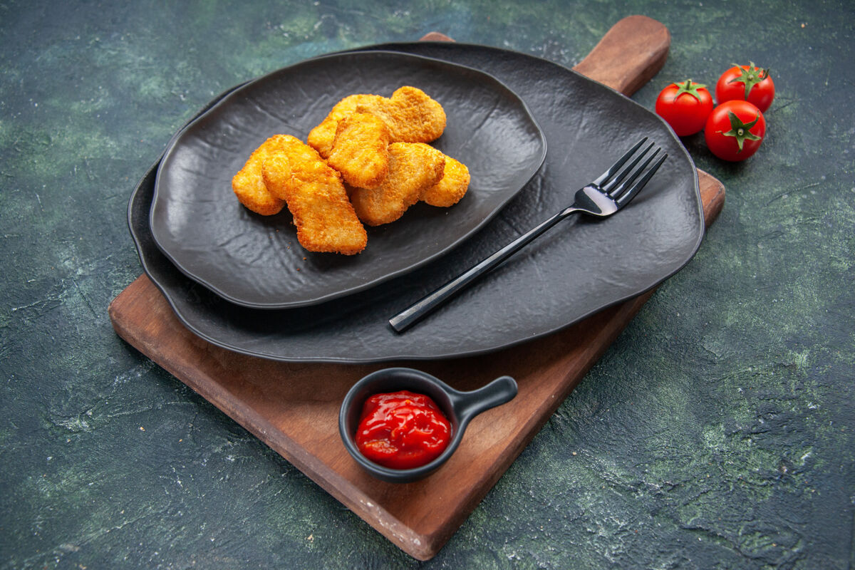 叉子把鸡块放在黑色的盘子里 叉子放在木板上 番茄酱放在深色的表面上烹饪容器食物