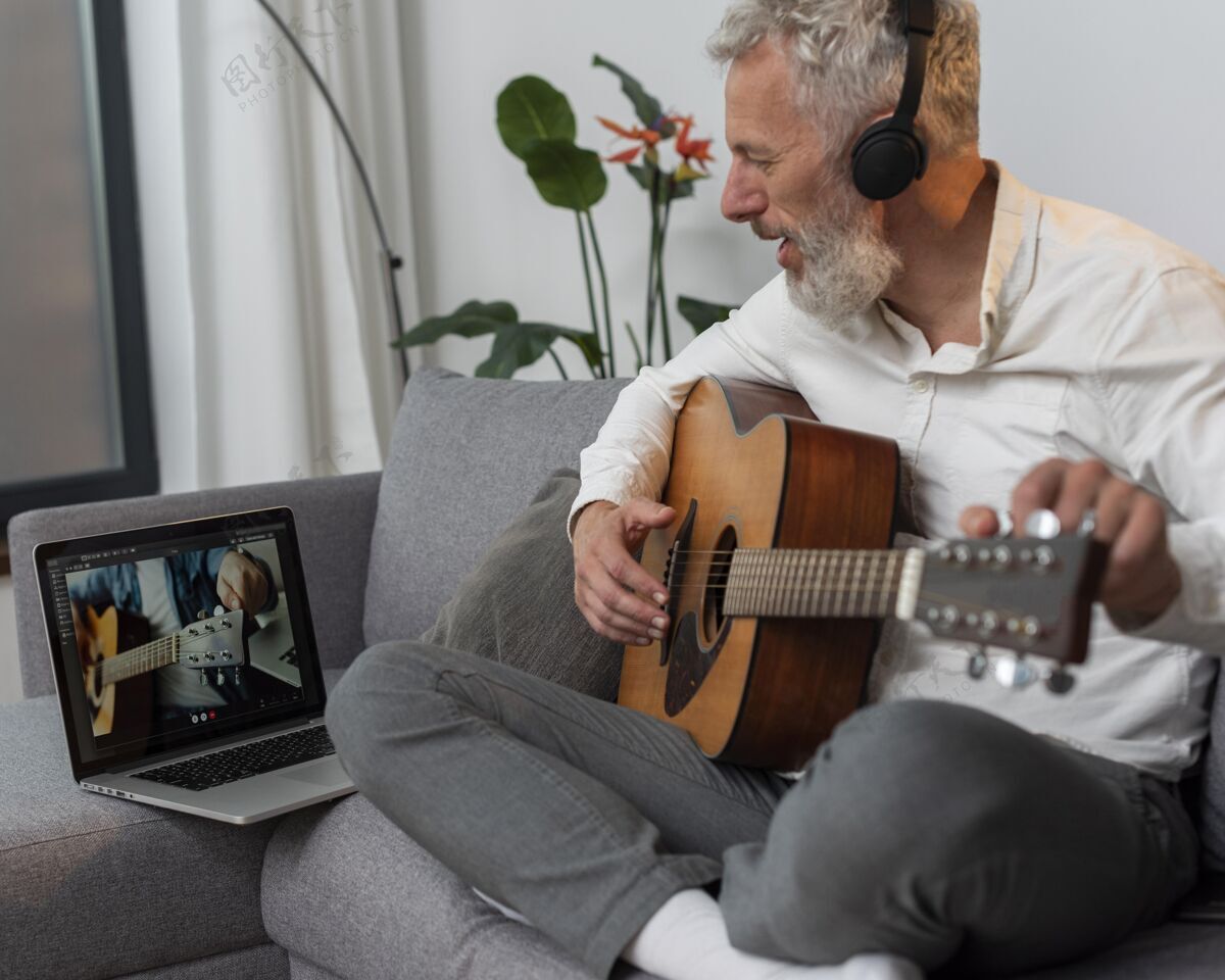 原声吉他老人在家的沙发上用笔记本电脑学习吉他课灰色头发老年人吉他课