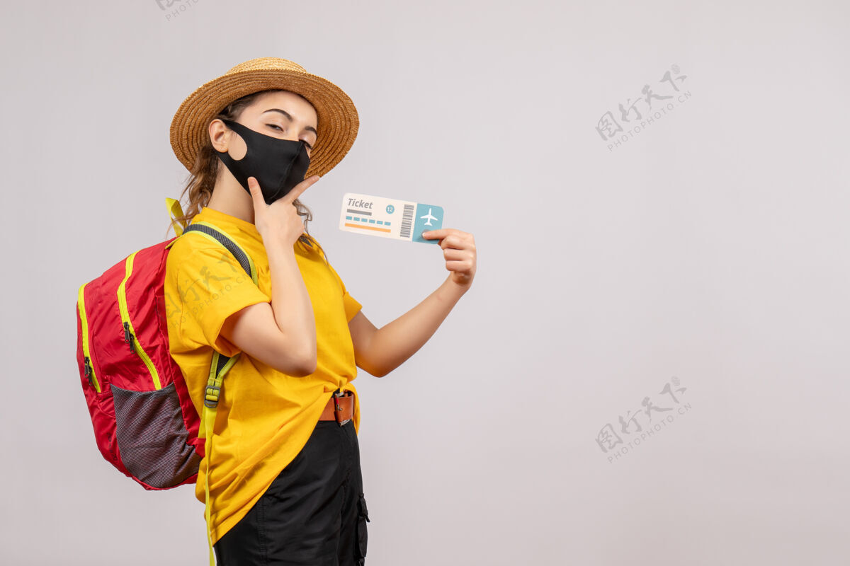 旅游正面图：年轻的旅行者背着背包 手放在下巴上举着车票面具背包面罩