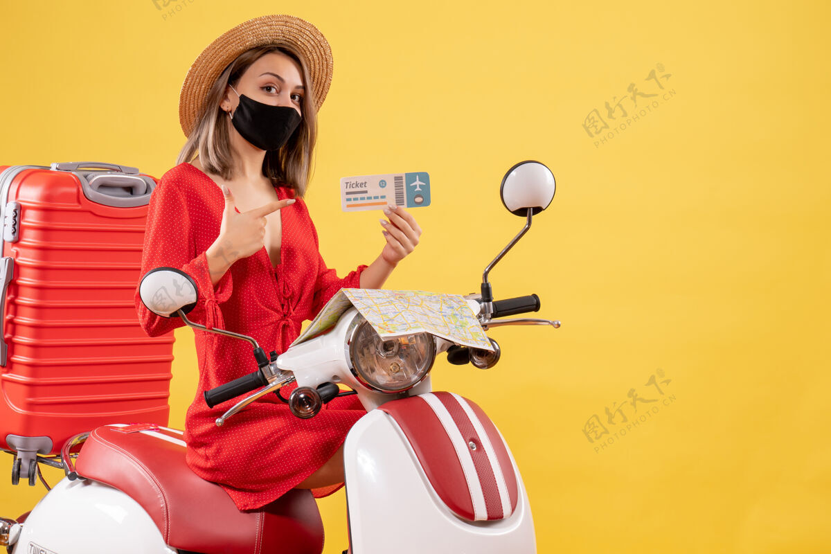车辆正面图：戴着黑色面罩的年轻女士坐在轻便摩托车上指着机票手提箱年轻女士游客