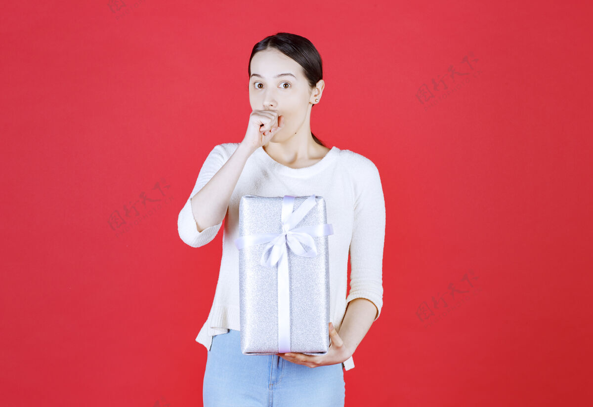 美丽红墙上拿着礼盒的震惊女人人脸礼物