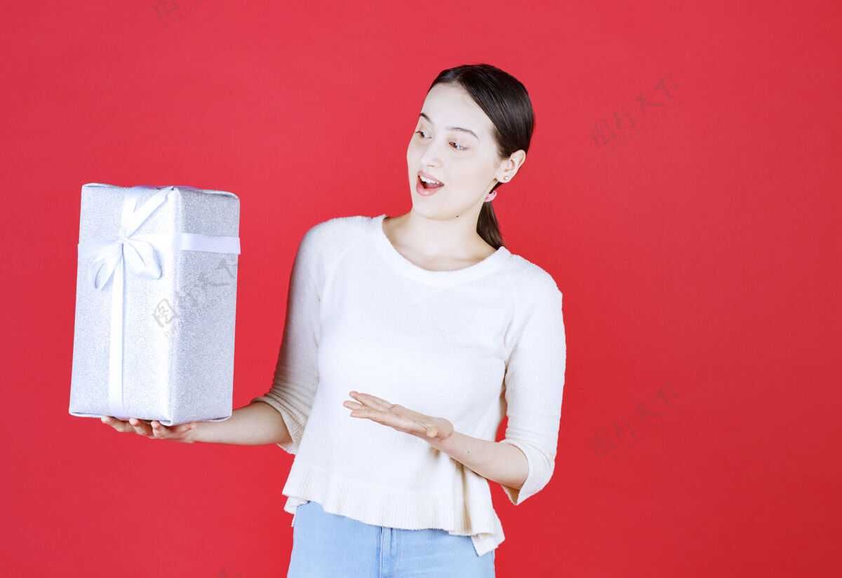 年轻年轻兴奋的女人拿着礼品盒指着手的肖像人头发微笑