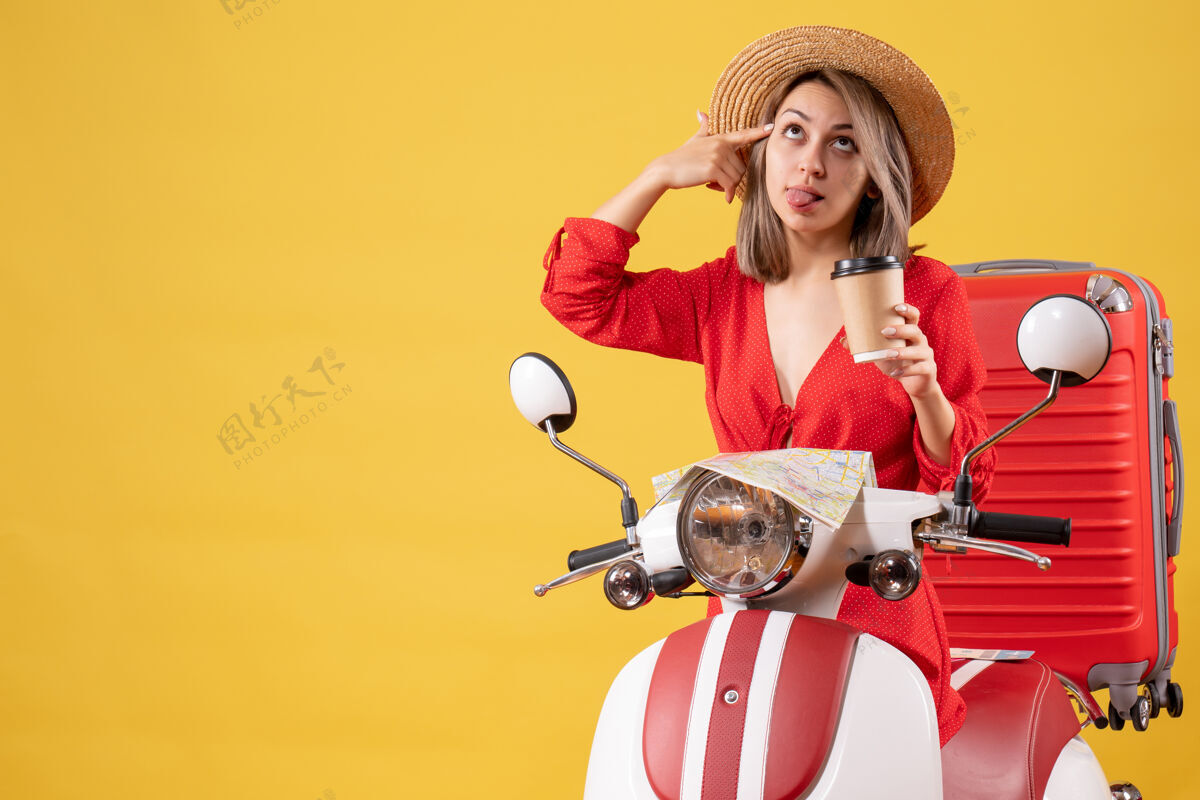 手势正面图：穿着红色连衣裙的年轻女士伸出舌头 拿着咖啡杯 靠近轻便摩托车舌头旅游肖像
