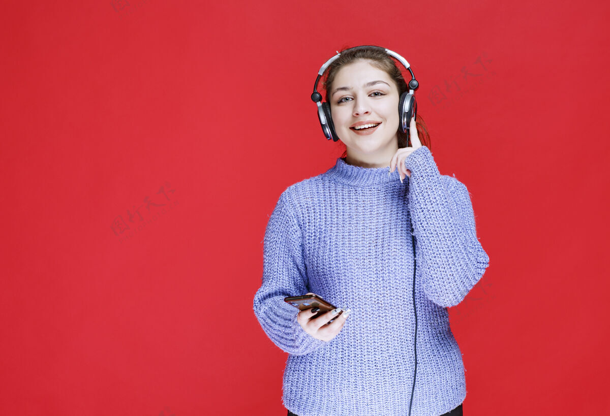 设备戴着耳机的女孩在她的智能手机上放音乐 享受着它满意服装员工