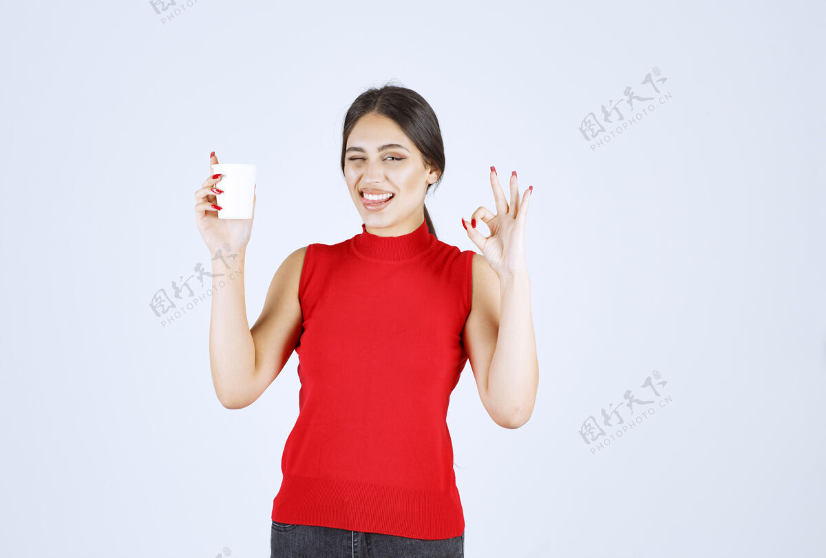 女人穿红衬衫的女孩在喝咖啡 并表现出积极的迹象姿势人员工