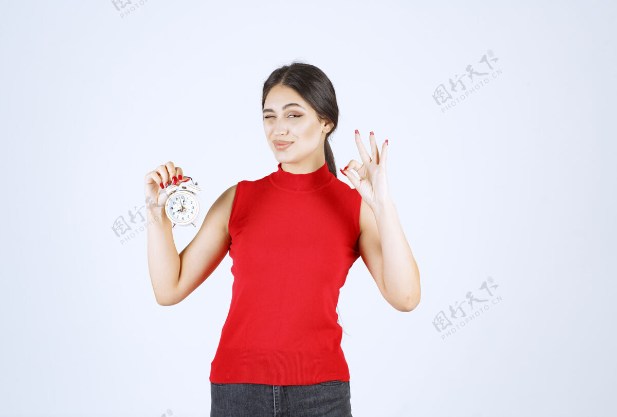 年轻穿着红衬衫的女孩拿着闹钟享受着产品好成功姿势