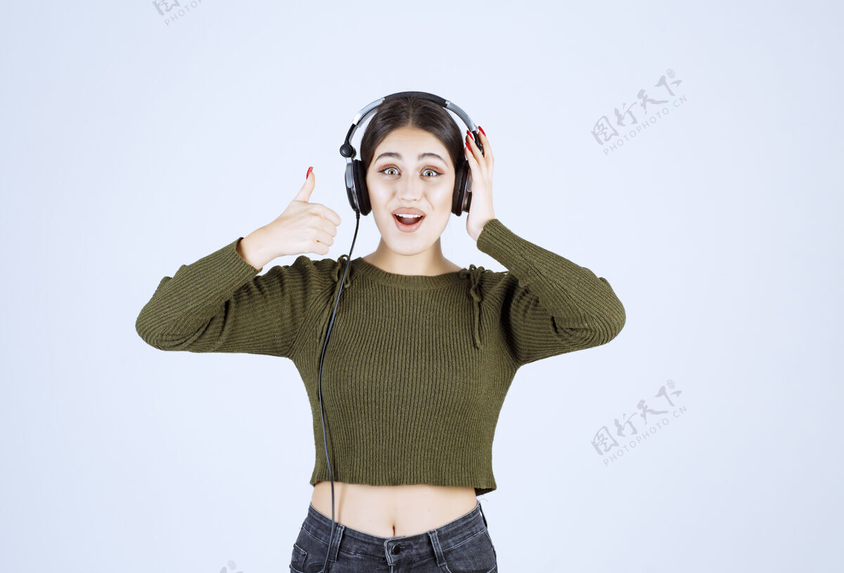 女孩戴着耳机听音乐竖起大拇指的年轻女孩的画像表达年轻音乐