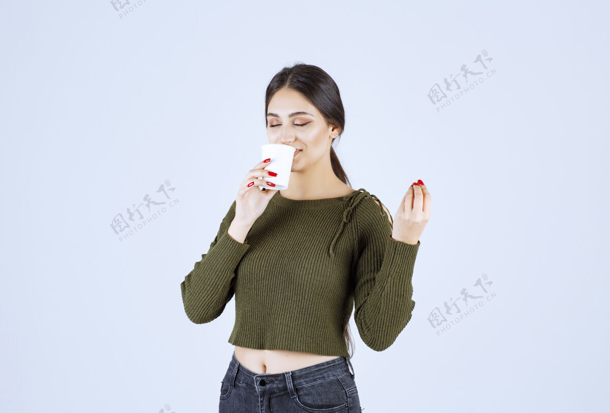 持有年轻的黑发女人喝着白色背景的塑料茶女人成人年轻