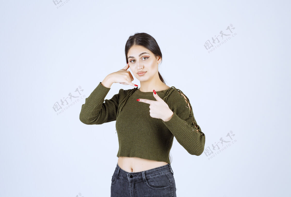 人类一个年轻漂亮的女模特正在做一个打电话的手势 并用食指指着一边指点女性目录