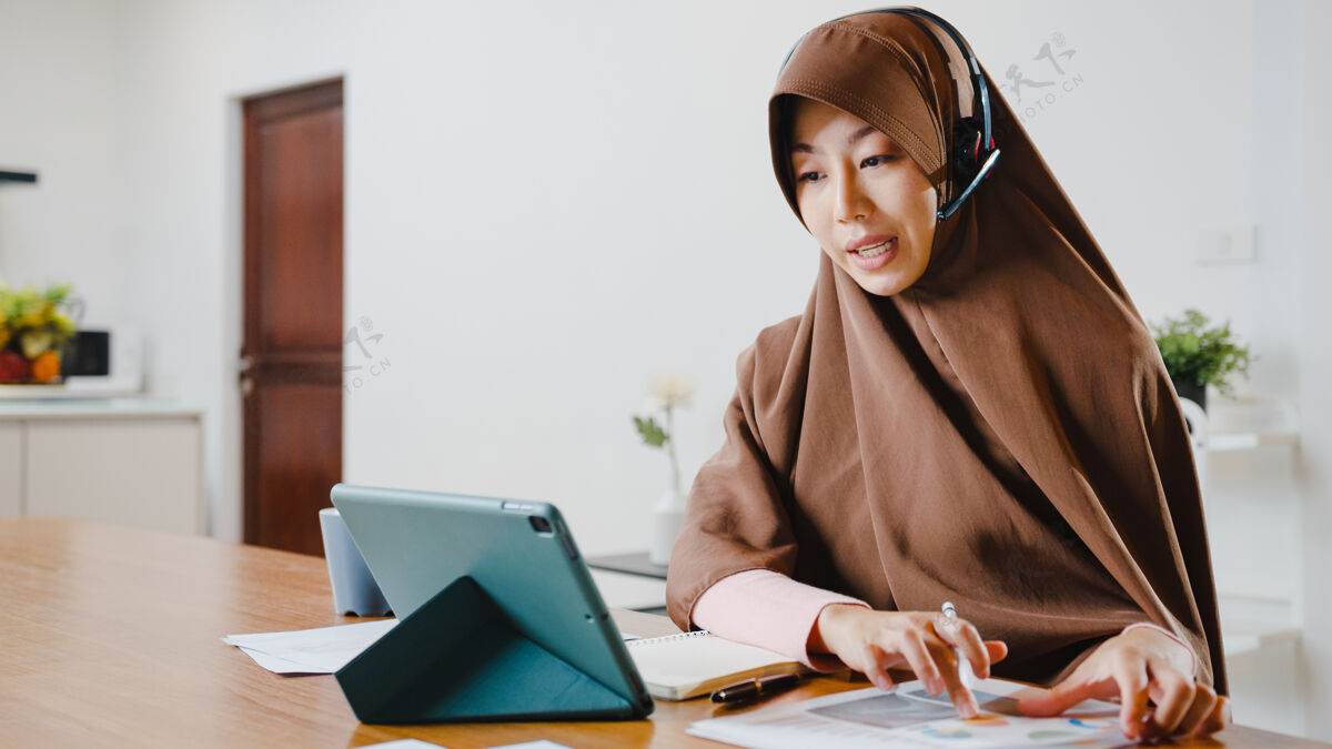 远程穆斯林女士戴着耳机使用数字平板电脑在家里厨房工作时 通过视频会议与同事谈论销售报告学生早晨耳机