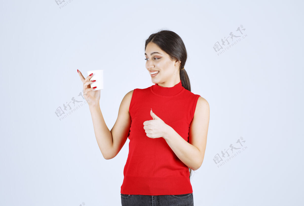 模特穿红衬衫的女孩在喝咖啡 并表现出积极的迹象喜欢成人品味