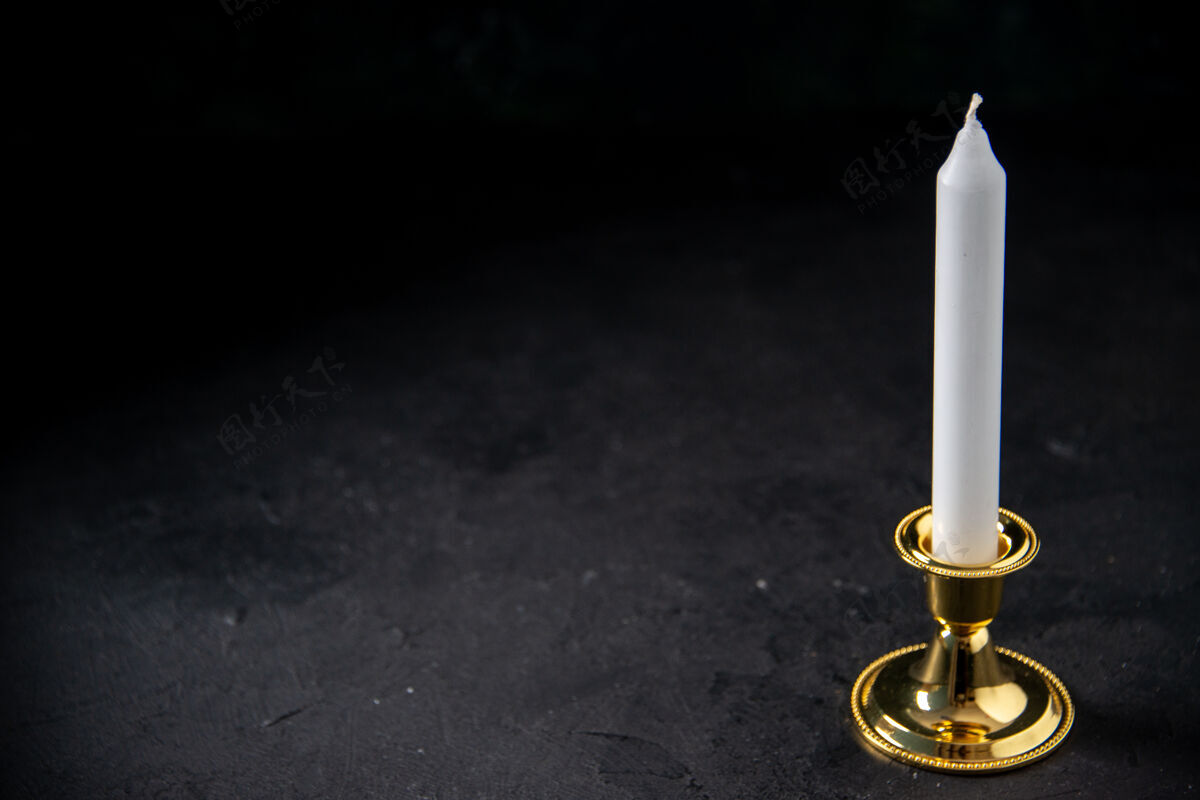 黑暗前视图中的白色蜡烛在黄金插入黑色火焰烛台火