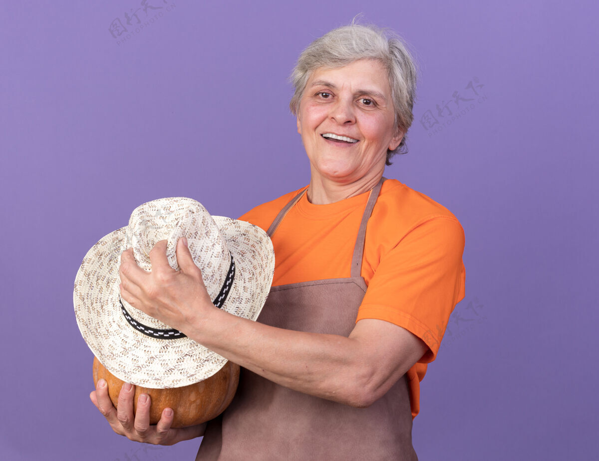 女微笑的上了年纪的女园丁拿着南瓜和园艺帽微笑帽子园艺