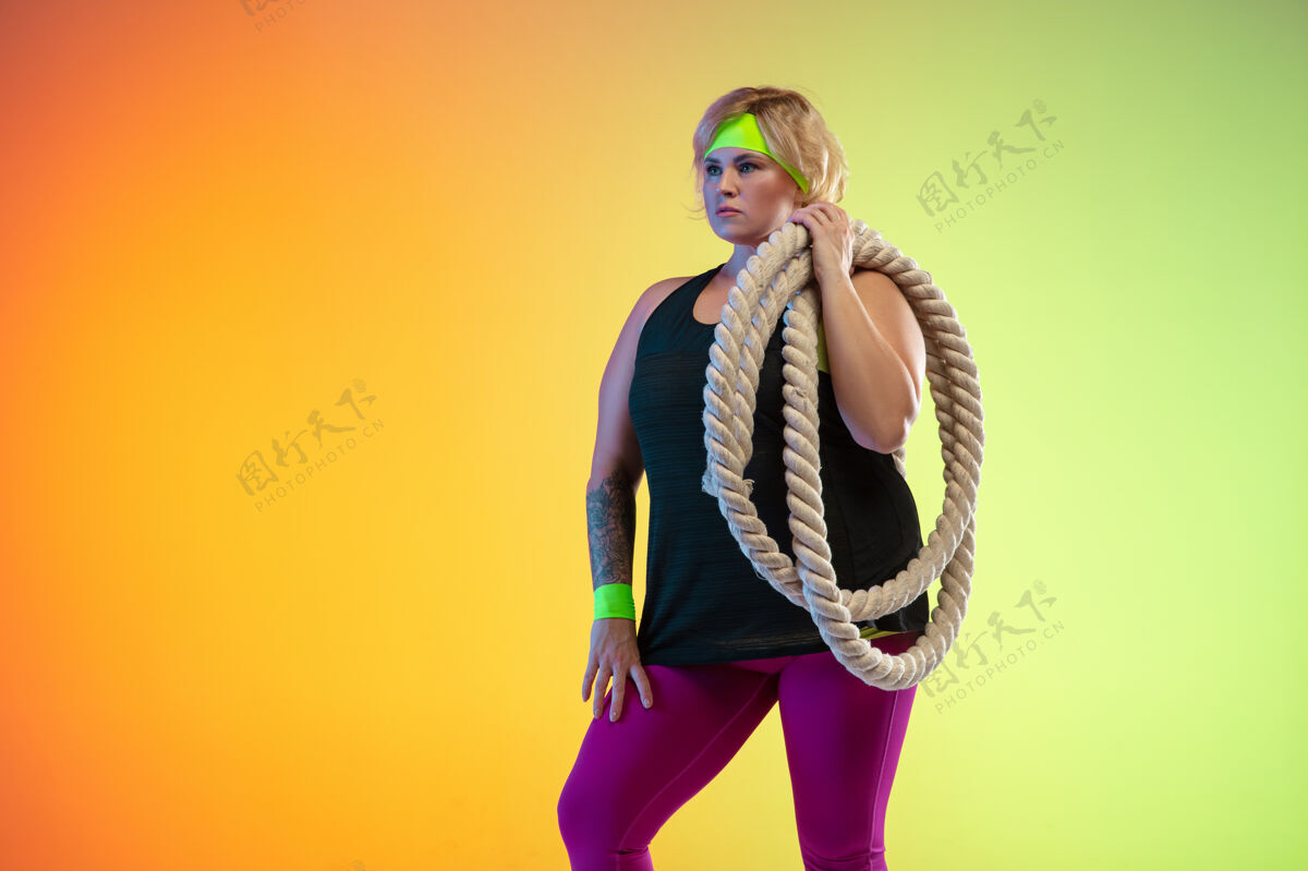 肖像年轻的白人大号女模特在霓虹灯下的橙色渐变背景上训练用绳子做锻炼运动的概念 健康的生活方式 积极的身体 平等护理女性健身房