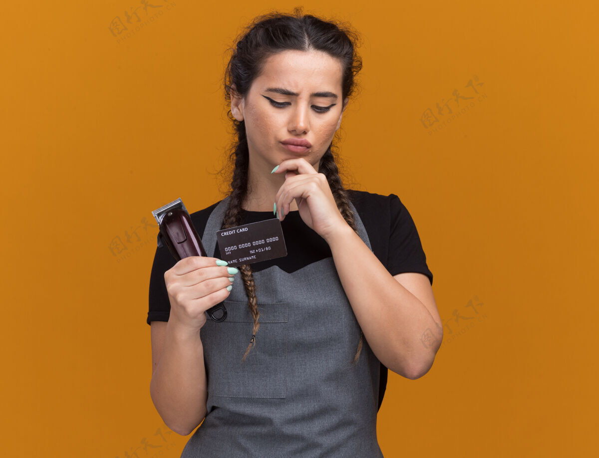 公民想着那个穿着制服的年轻女理发师 手里拿着一张信用卡 手里拿着一把剪子 把下巴贴在橘色的墙上女性表情剪子