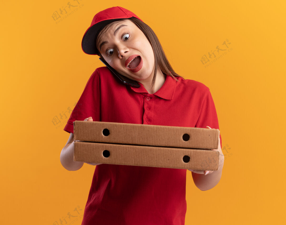 漂亮穿着制服的焦急漂亮的女送货员在打电话 手里拿着比萨饼盒橘子送货女人