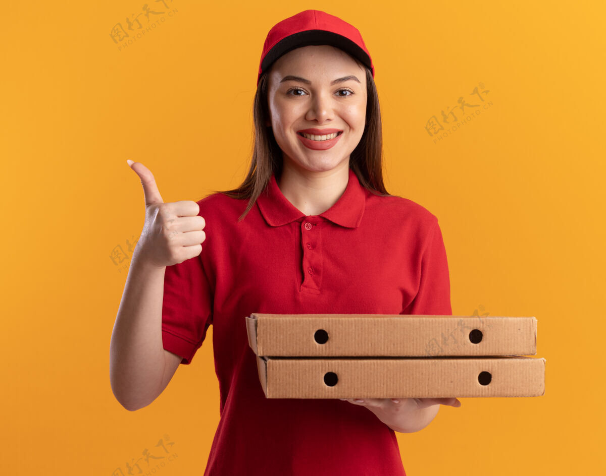 拇指微笑着的漂亮的送货员 穿着制服 竖起大拇指 拿着比萨饼盒女人拿着橘子