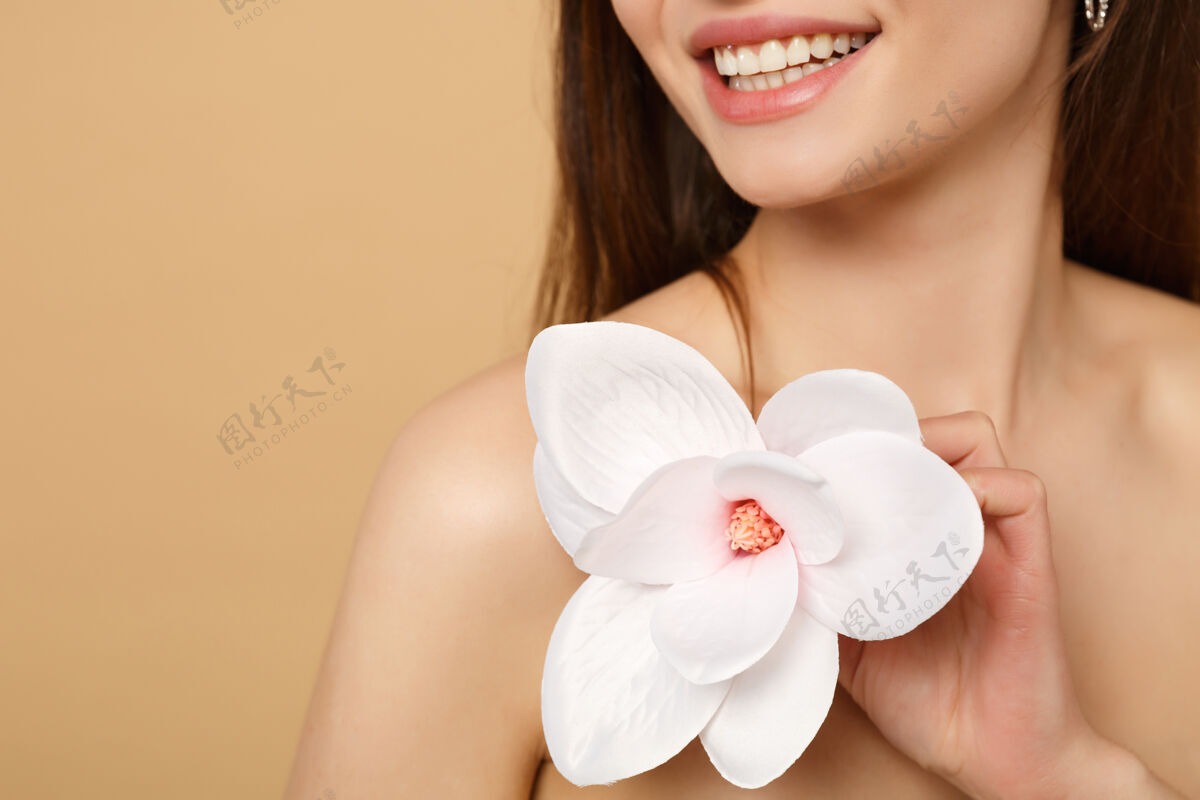 头发特写黑发半裸女人完美的皮肤 裸妆隔离在米色粉彩墙上兰花开花提举