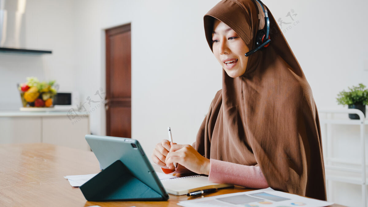 商务女性穆斯林女士戴着耳机使用数字平板电脑在家里厨房工作时 通过视频会议与同事谈论销售报告社交房子厨房