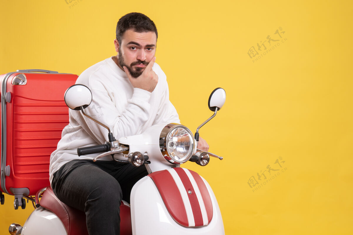 微笑顶视图自信的年轻人坐在摩托车上 手提箱放在孤立的黄色背景上摩托车成人培训