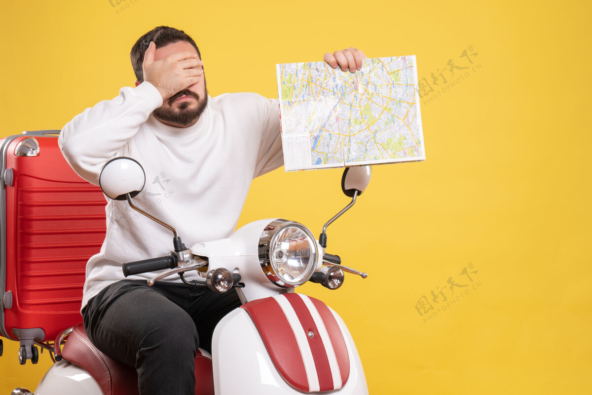 摩托车俯视图是一个情绪激动的家伙坐在摩托车上 手提箱放在上面 拿着地图 背景是孤立的黄色背景手提箱微笑
