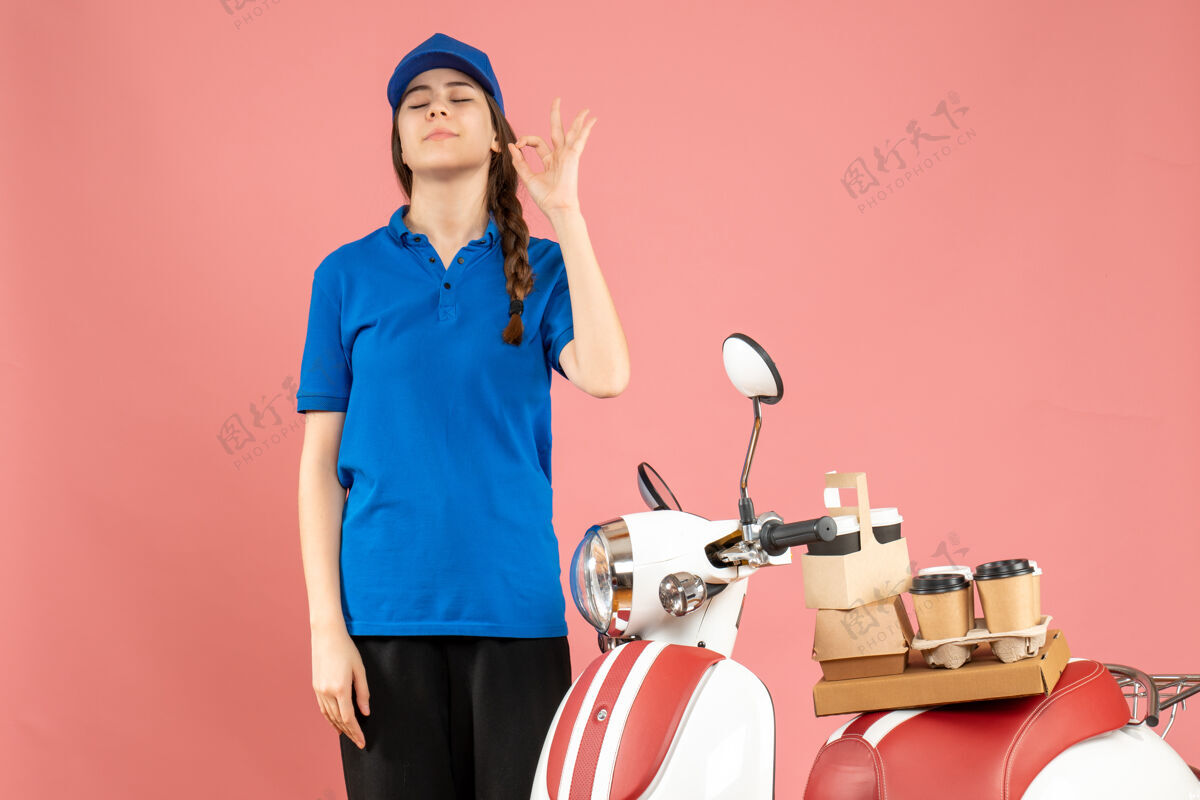 站俯视图：信使女士站在摩托车旁边 车上有咖啡和小蛋糕 在柔和的桃色背景上做眼镜手势护士蛋糕粉彩