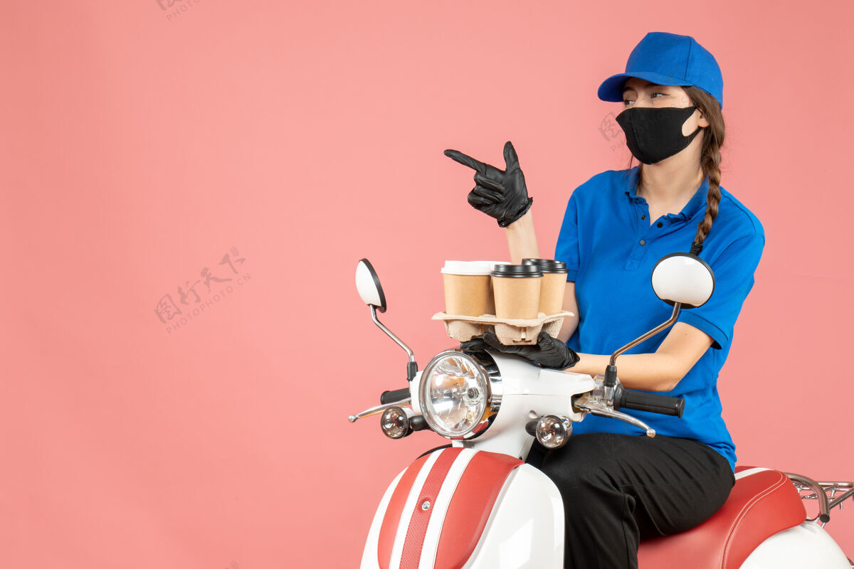 粉彩前视图困惑的女性送货员戴着医用面罩和手套坐在滑板车上举行粉彩桃背景命令举行男前面