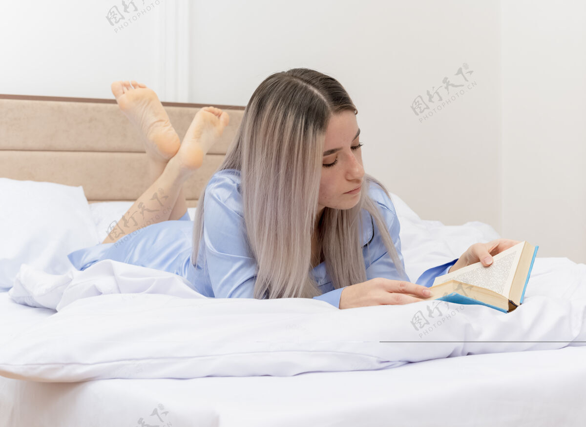 灯光穿着蓝色睡衣的年轻美女躺在床上 在卧室里看书休息漂亮阅读