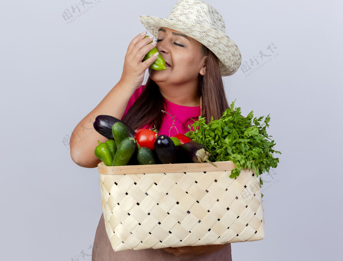 香味中年女园丁围着围裙 戴着帽子 拿着装满蔬菜的板条箱 感受着新鲜甜椒的芳香铃铛新鲜的板条箱