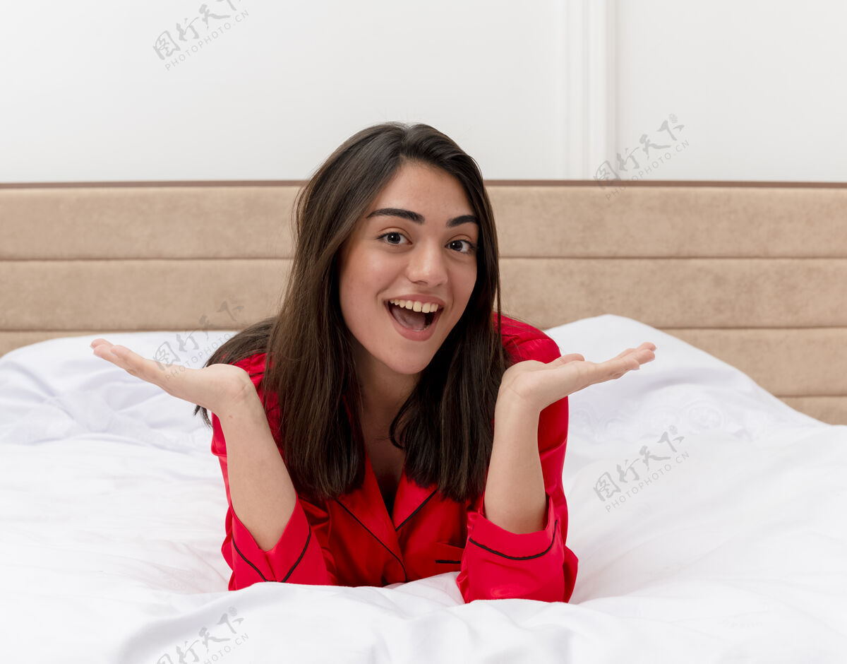 背景穿着红色睡衣的年轻美女躺在床上放松 笑容可掬室内卧室背景漂亮女人年轻